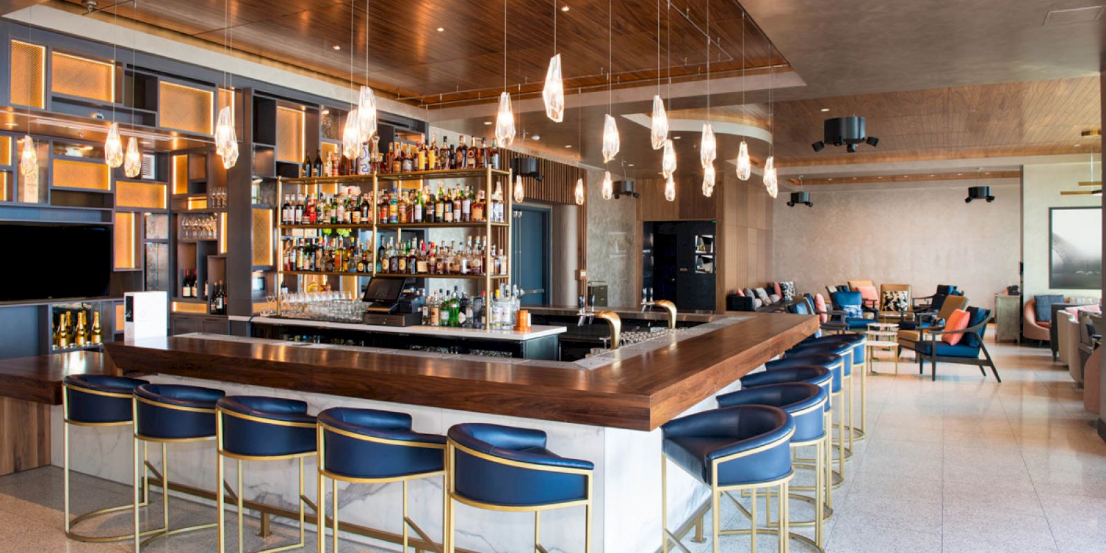 This image shows a modern bar with stylish seating, pendant lights, and a well-stocked back bar in a spacious lounge setting.