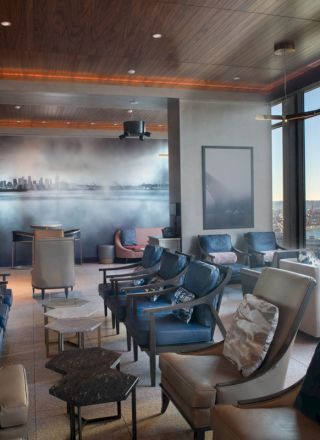 A modern lounge with comfortable seating, large windows with a city view, and ambient lighting.