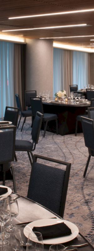 The image shows an elegantly set banquet hall with round tables, dark chairs, dishes, and floral centerpieces, ready for an event.