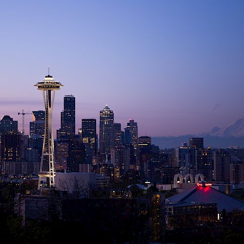 Seattle skyline at dusk with the Space Needle, downtown buildings, and Mount Rainier in the background.