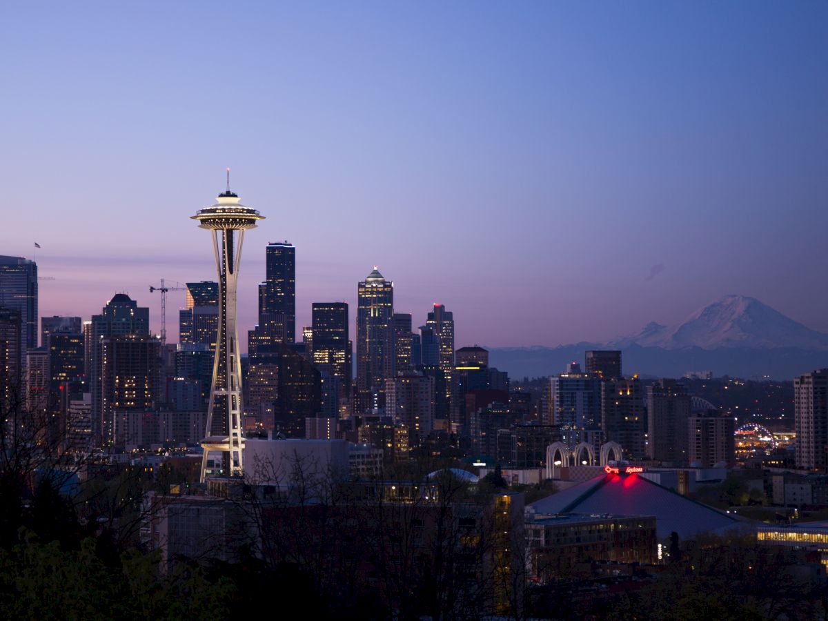 The image shows a city skyline at dusk with a prominent tower and a distant mountain under a purple sky.