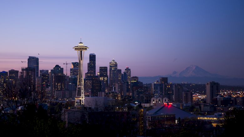 The image shows a city skyline at dusk with a prominent tower and a distant mountain under a purple sky.